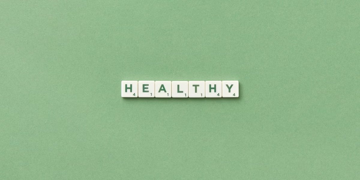 Scrabble tiles spelling the word 'healthy' on a light green background, top view.