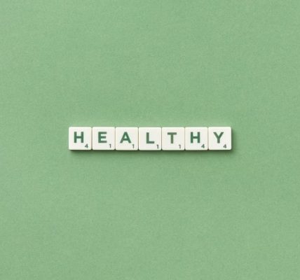 Scrabble tiles spelling the word 'healthy' on a light green background, top view.