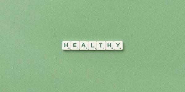 Scrabble tiles spelling the word 'healthy' on a light green background, top view.