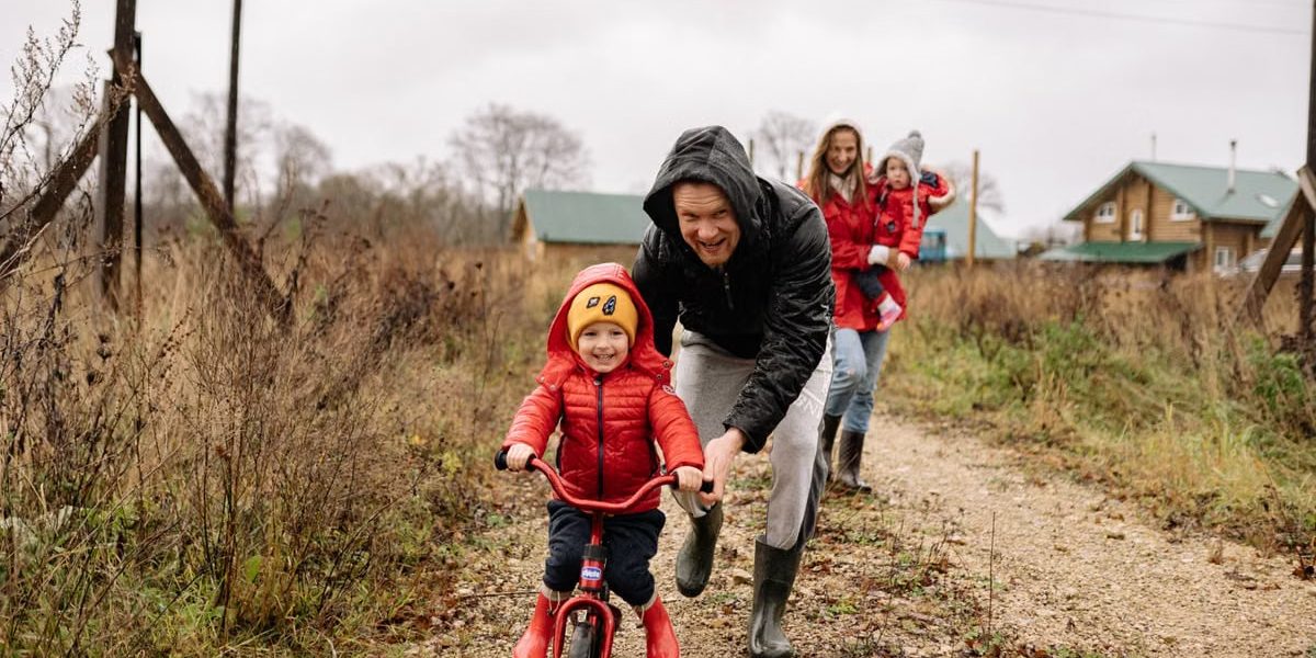 A happy family enjoys a bonding moment outdoors with a child learning to ride a bicycle on a fall day.