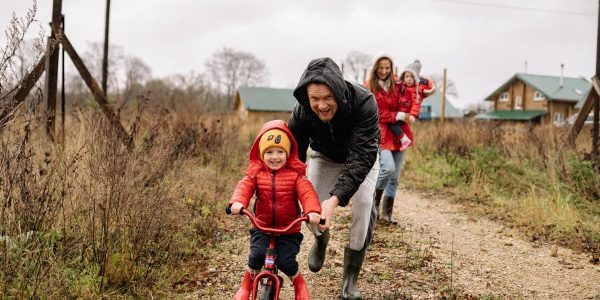 A happy family enjoys a bonding moment outdoors with a child learning to ride a bicycle on a fall day.