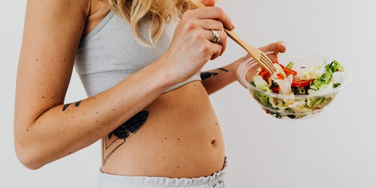 Close-up of a woman in a crop top enjoying a fresh salad indoors.
