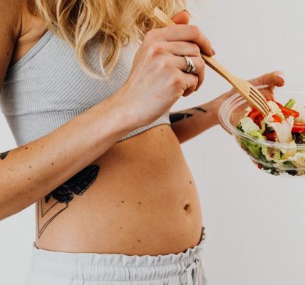 Close-up of a woman in a crop top enjoying a fresh salad indoors.